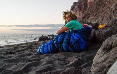 Man sitting on rock at beach against sky