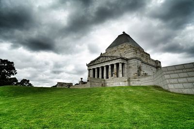 Historic building on field against cloudy sky