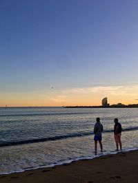 Friends on beach against sky during sunset