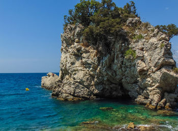 Rock formation in sea against clear blue sky