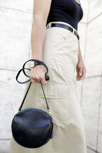 Woman holding bag while standing against wall