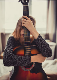 Woman hiding face with guitar at home