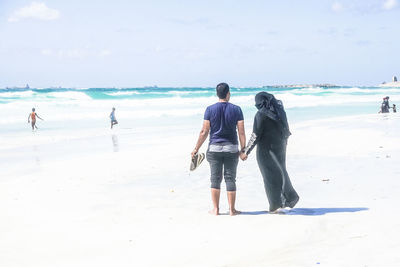 Rear view of men walking on beach against sky