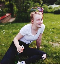 Smiling teenage girl holding bottle while sitting on grass