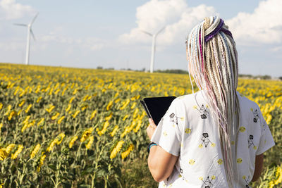 Woman, tablet in field sunflowers, wind turbines for green energy production, eco-energy, wind 