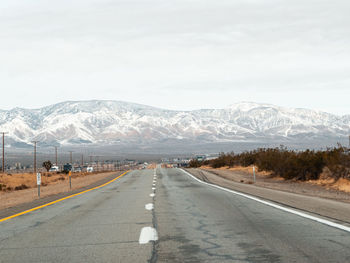 Road by snowcapped mountains against sky