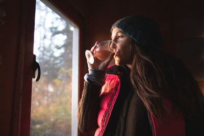 Young woman having drink by window at home