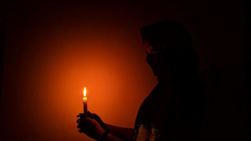 Woman holding illuminated candle in darkroom