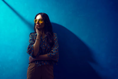 Woman standing by swimming pool against blue wall