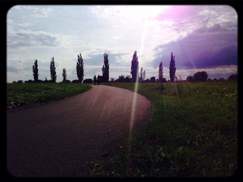 Road passing through field against cloudy sky