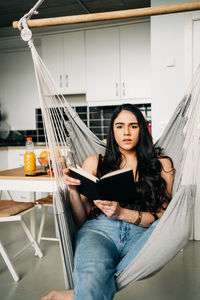 Portrait of young woman sitting on hammock at home