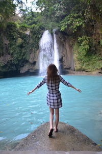 Rear view of woman by waterfall at forest