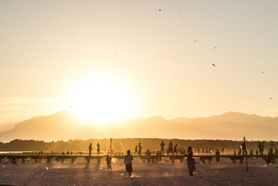 People enjoying at beach against sky during sunset