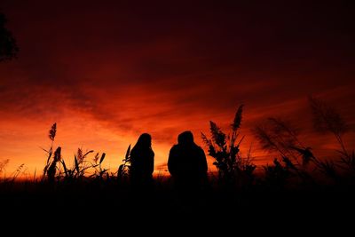 Silhouette people standing on field against orange sky