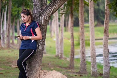 Full length of young woman using phone on tree