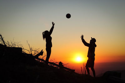 Silhouette people playing with ball against sky during sunset