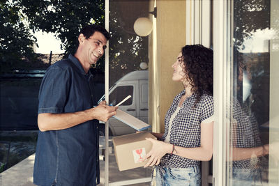 Smiling delivery man talking to woman against house