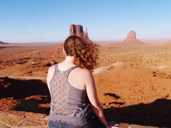 Rear view of woman sitting on retaining wall at desert against clear sky