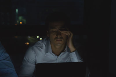 Tired businessman rubbing eyes while working late in office at night