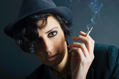 Portrait of confident young woman smoking cigarette against wall