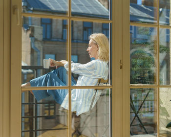 Happy elderly woman sitting on terrace with cup of coffee and enjoying sunny morning