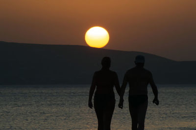 Rear view of silhouette man standing in sea against sky during sunset