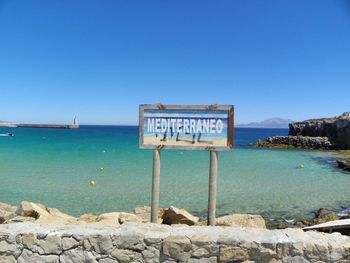 Information sign on rocks by mediterranean sea against clear sky