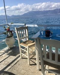 Chairs and table by sea against sky