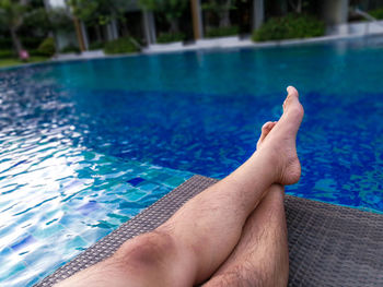 Low section of man relaxing at swimming pool