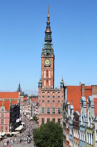 Clock tower by buildings against clear blue sky in city