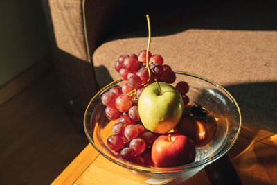 Glass bowl of variety of fruits on wooden table in warm sun light.