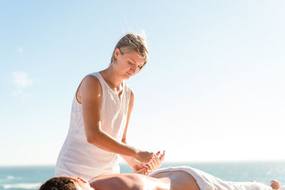 Side view of young woman exercising against sky