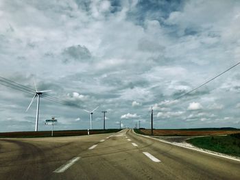 Road by electricity pylon against sky