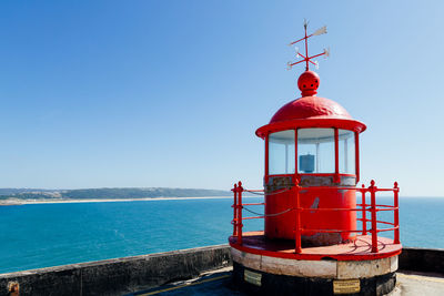 Lighthouse by sea against clear blue sky