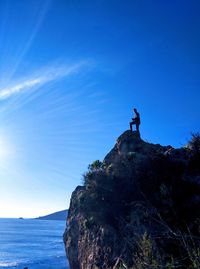 Man standing on beach cliff against blue sky