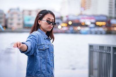 Young woman wearing sunglasses standing by railing in city