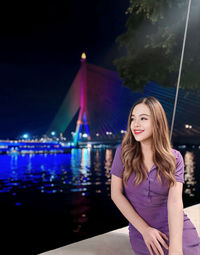 Portrait of young woman standing against illuminated city at night