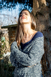 Young woman with closed eyes standing against tree during sunny day