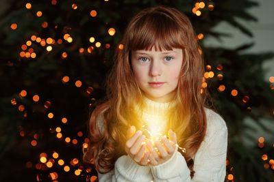 Happy young girl sitting by the christmas tree with garland