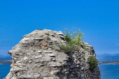 Rock formation by sea against clear blue sky