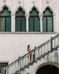 Side view of stylish young woman walking on stairs of beautiful old building in city.