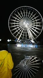 Rear view of woman standing by illuminated ferris wheel at night