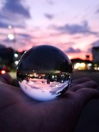 Close-up of hand holding crystal ball against sky during sunset