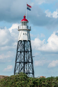 Lighthouse construction by sea against sky with dutch flag