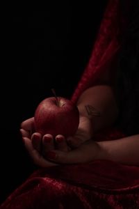 Close-up of hand holding strawberry over black background