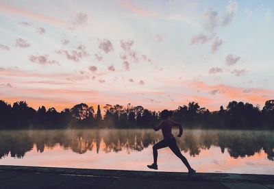 Reflection of man in lake against sky during sunset