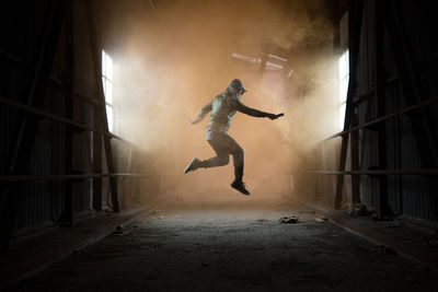 Full length of man holding distress flare while jumping in abandoned workshop