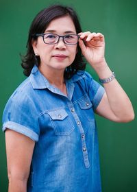 Portrait of confident teacher wearing eyeglasses against green chalkboard