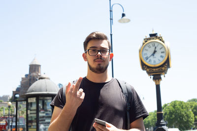 Portrait of young man standing against clock tower