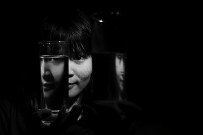 Close-up portrait of young woman looking through drinking glass against black background